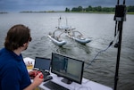 Raymond Koehler, a mechanical engineer at the Naval Air Warfare Center Aircraft Division, demonstrates unmanned swarm mission planning software at Naval Air Station Patuxent River’s West Basin Marina in Md. on June 17, 2025. The software helps the Navy plan missions with unmanned systems by simulating drone, sensor, and arrangement combinations to achieve mission goals at sea ultimately providing warfighters faster and more effective decision making. (U.S. Navy photo by Todd Frantom)
