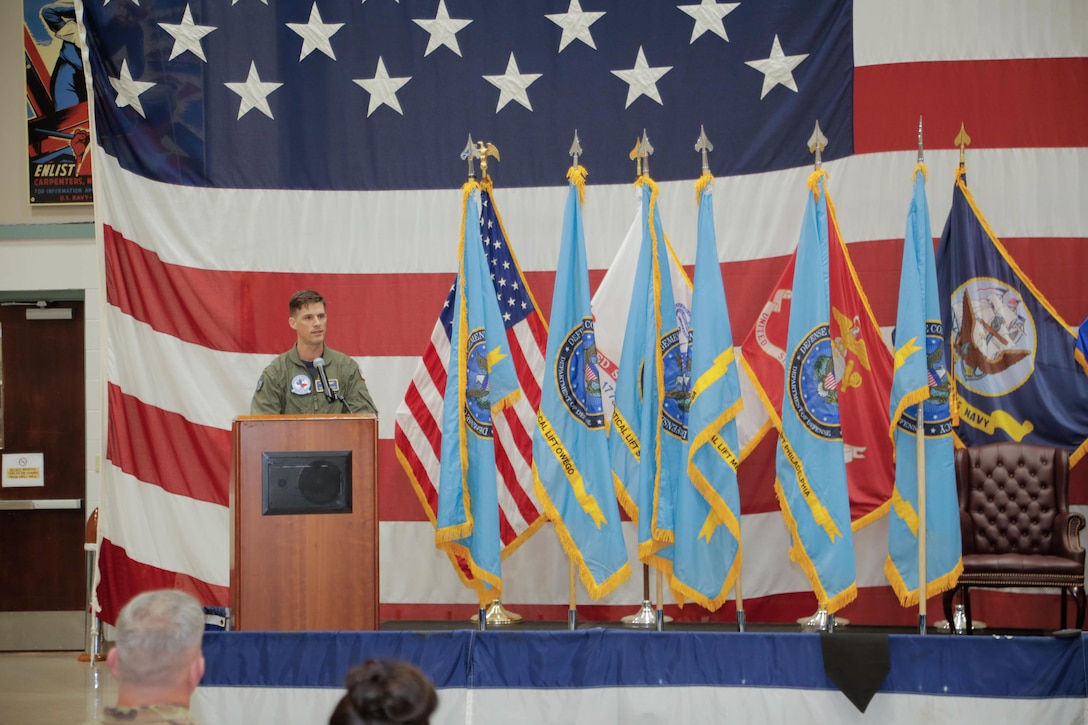 A male in a flight suit stands at a podium