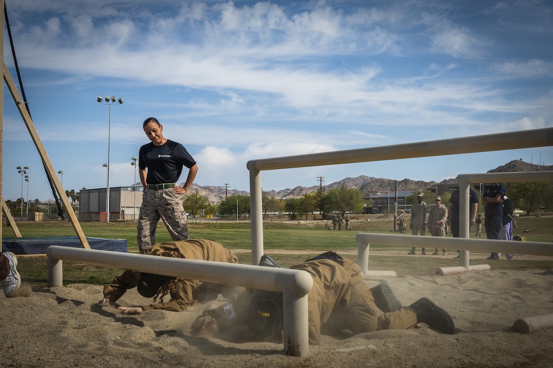 U.S. Marine Corps Staff Sgt. Amber Kelly, facilities chief with Headquarters Battalion, Marine Air Ground Task Force Training Command, Marine Corps Air Ground Combat Center supervises as Morongo Unified School District students navigate an obstacle course during a Military Occupational Specialty Exposition at Marine Corps Air Ground Combat Center, Twentynine Palms, California, May 1, 2025. The students move over and under obstacles, to experience military training. (U.S. Marine Corps photo by Pfc. Dominic Spence)