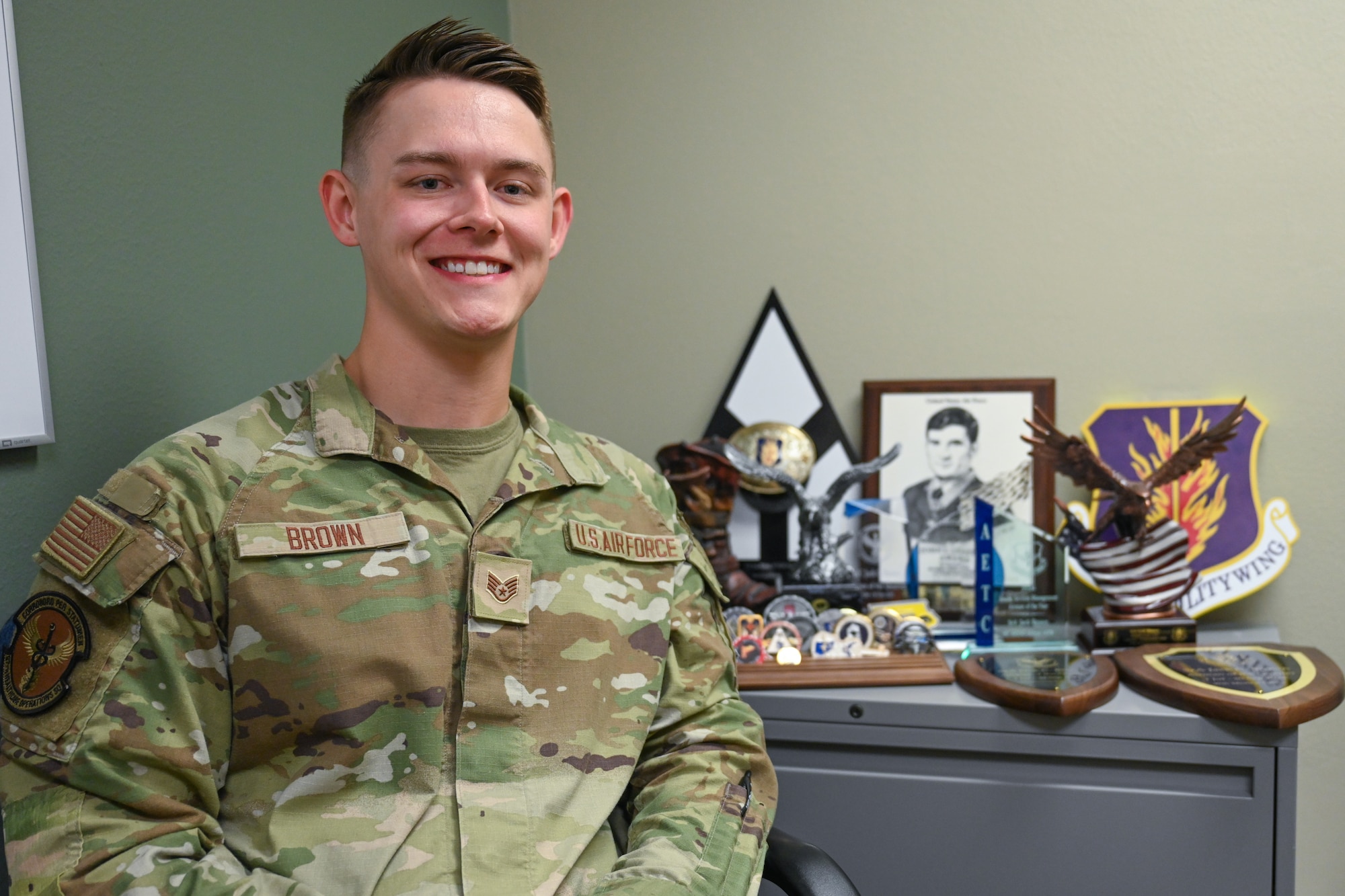 U.S. Air Force Staff. Sgt. Jack Brown, 97th Healthcare Operations Squadron TRICARE operations and patient administration non-commissioned officer in charge, poses by his coins and numerous trophies at Altus Air Force Base, Oklahoma, May 28, 2025. Brown was selected to compete for the top 9 Outstanding Airmen of the Year in Washington, D.C. (U.S. Air Force photo by Airman 1st Class Nathan Langston)