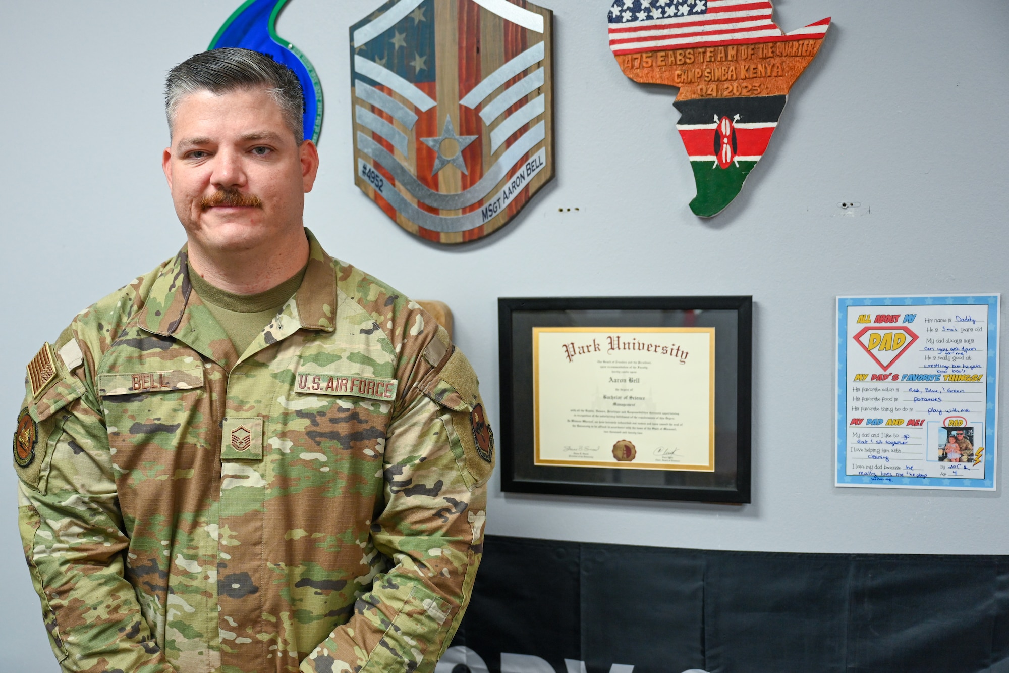 U.S. Air Force Master Sgt. Aaron Bell, 97th Logistics Readiness Squadron vehicle fleet manager, stands by his mounted awards and degree at Altus Air Force Base, Oklahoma, May 20, 2025. Bell credits his achievements to his high efforts and positive attitude. (U.S. Air Force photo by Airman 1st Class Nathan Langston)