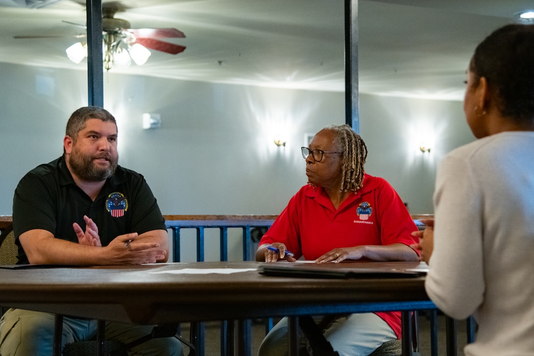 A man and woman sit at a table looking across the table at another person.