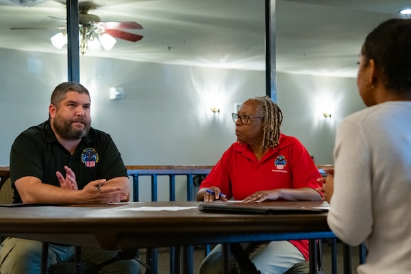 A man and woman sit at a table looking across the table at another person.