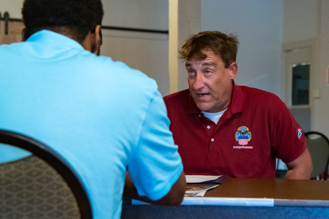 A man sits at a table looking across the table at another person.