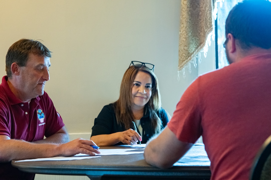 A man and woman sit at a table looking across the table at another person.