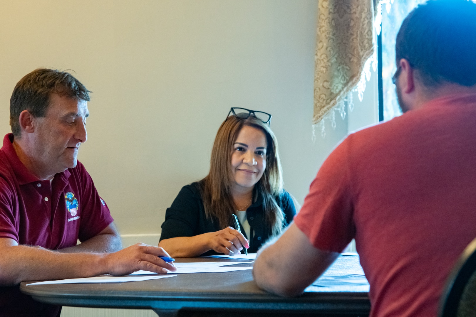 A man and woman sit at a table looking across the table at another person.