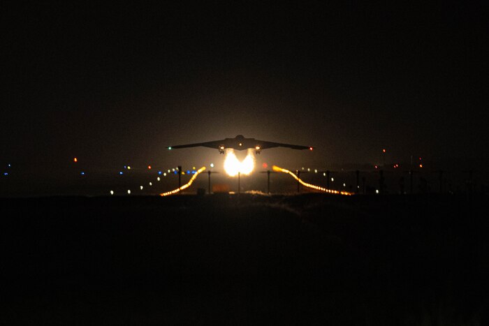 The silhouette of a military aircraft taking off at night with fire trailing behind it.