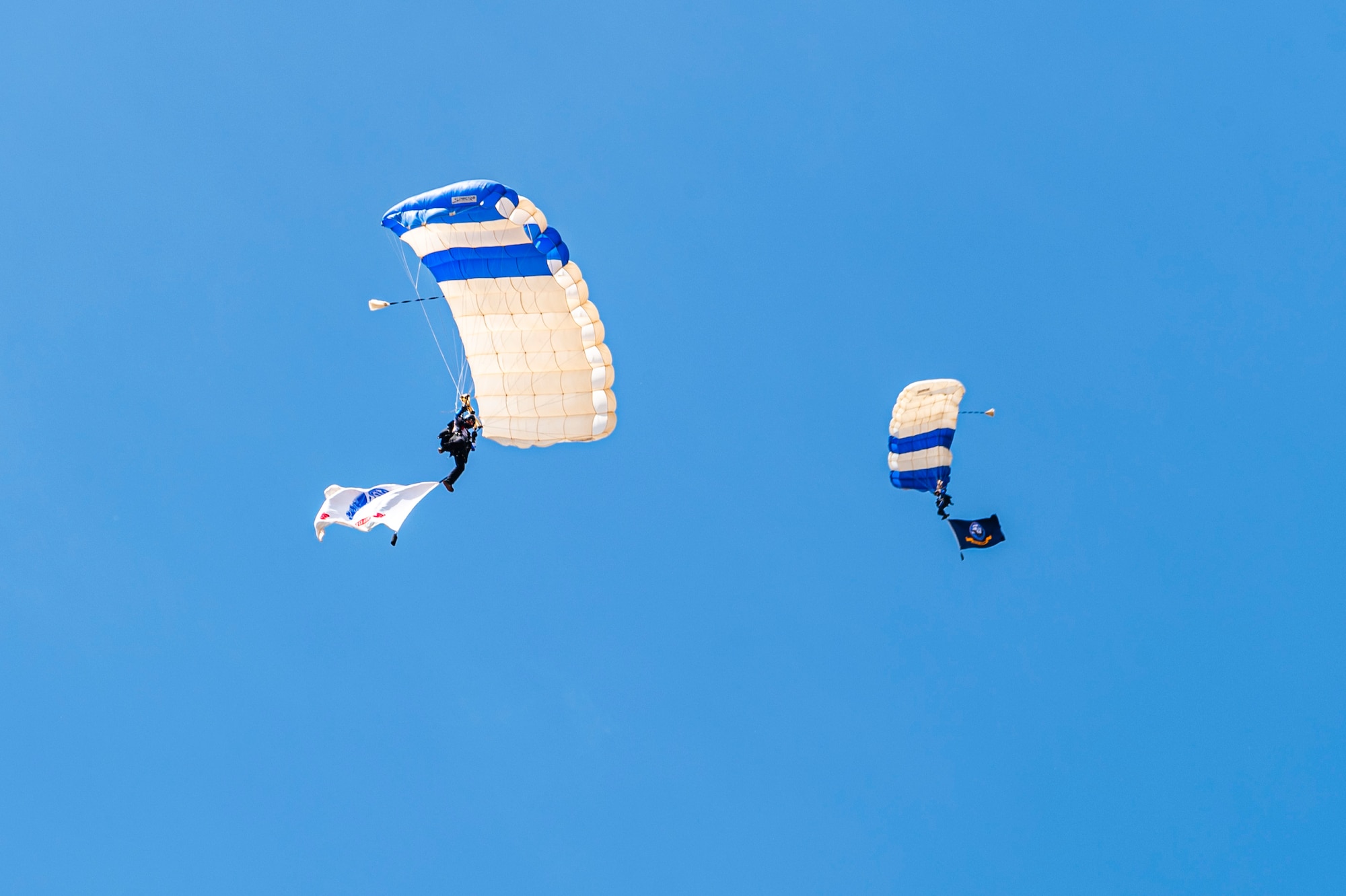 U.S. Air Force Tech. Sgt. Robert Tolli, 98th Flying Training Squadron Airmanship 490 course director, left, and First-Class Cadet Colin Laughrey, 98th FTS Wings of Blue demonstrator, display the U.S. Army and Navy flags while parachuting during the 2025 Moses Lake Airshow at Grant County International Airport, Washington, June 20, 2025.