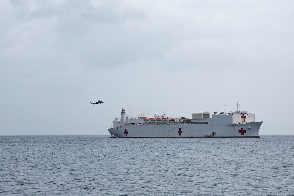 A white U.S. military hospital ship floats in the ocean while a military helicopter approaches it