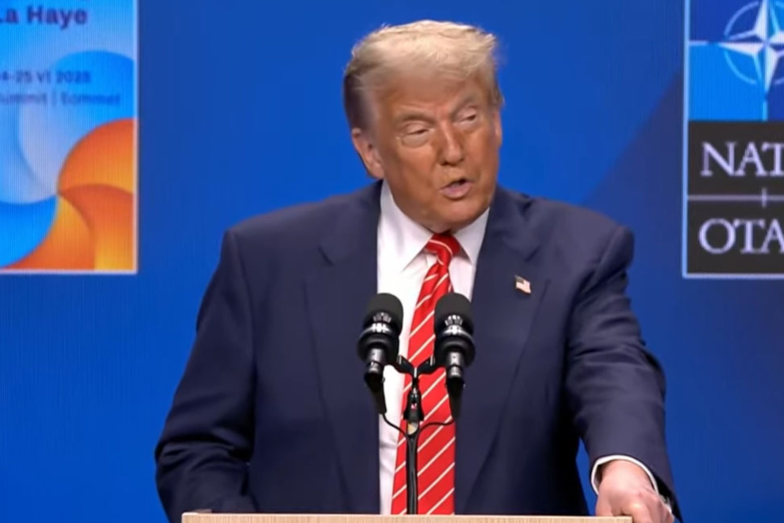 A man in a suit and tie speaks in front of a lectern.