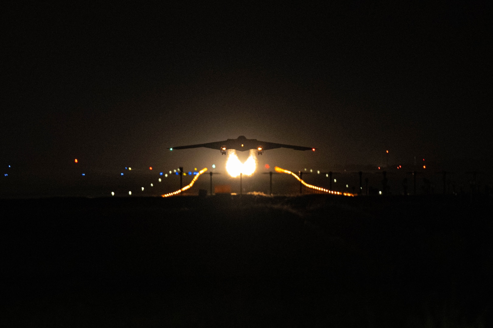 The silhouette of a military aircraft taking off at night with fire trailing behind it.