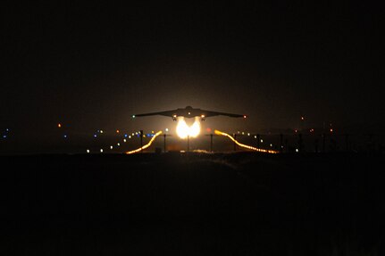 The silhouette of a military aircraft taking off at night with fire trailing behind it.
