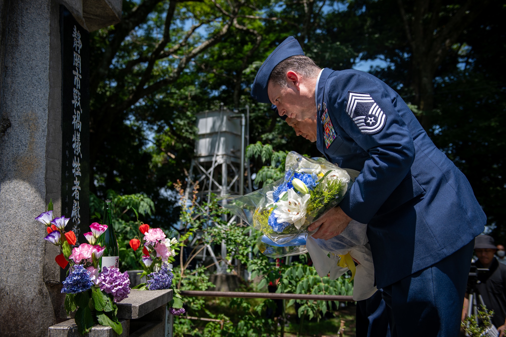 An Airman dressed in their blue dress uniform performs the action of laying colorful flowers at the foot of a stone monument.