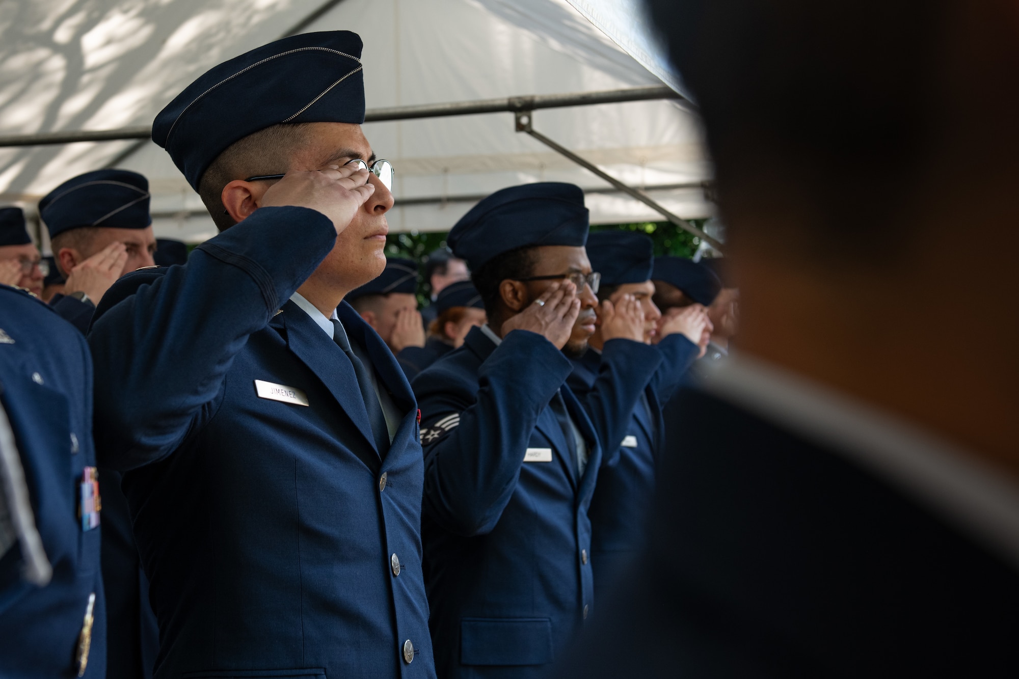 A group of Airmen dressed in their blue dress uniforms and flight caps, render salutes during the presentation of the colors.