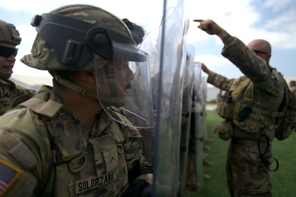 U.S. Army Pvt. Arnoldo Solorzano, a cavalry scout with Troop A, 1st Squadron, 18th Cavalry Regiment, California Army National Guard, watches through his riot shield as U.S. Army Sgt. Jose Benitz, from the same unit, reviews proper positioning and movement techniques during training on riot and crowd control procedures at Joint Forces Training Base Los Alamitos, California, on June 22, 2025.