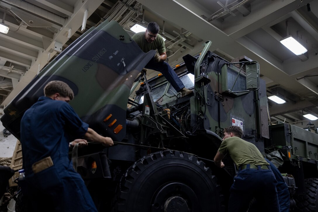U.S. Marines with Combat Logistics Battalion 26, 22nd Marine Expeditionary Unit (Special Operations Capable), conduct routine maintenance on a medium tactical vehicle replacement during Composite Training Unit Exercise, aboard the San Antonio-class amphibious transport dock ship USS San Antonio (LPD 17), Iwo Jima Amphibious Ready Group, while underway in the Atlantic Ocean, June 24, 2025. During COMPTUEX, the IWOARG and 22nd MEU (SOC) refine tactics, techniques, and procedures to execute warfighting functions that enhance operational readiness and lethality as a unified IWOARG/22 MEU (SOC) team. (U.S. Marine Corps photo by Lance Cpl. Kyle Baskin)