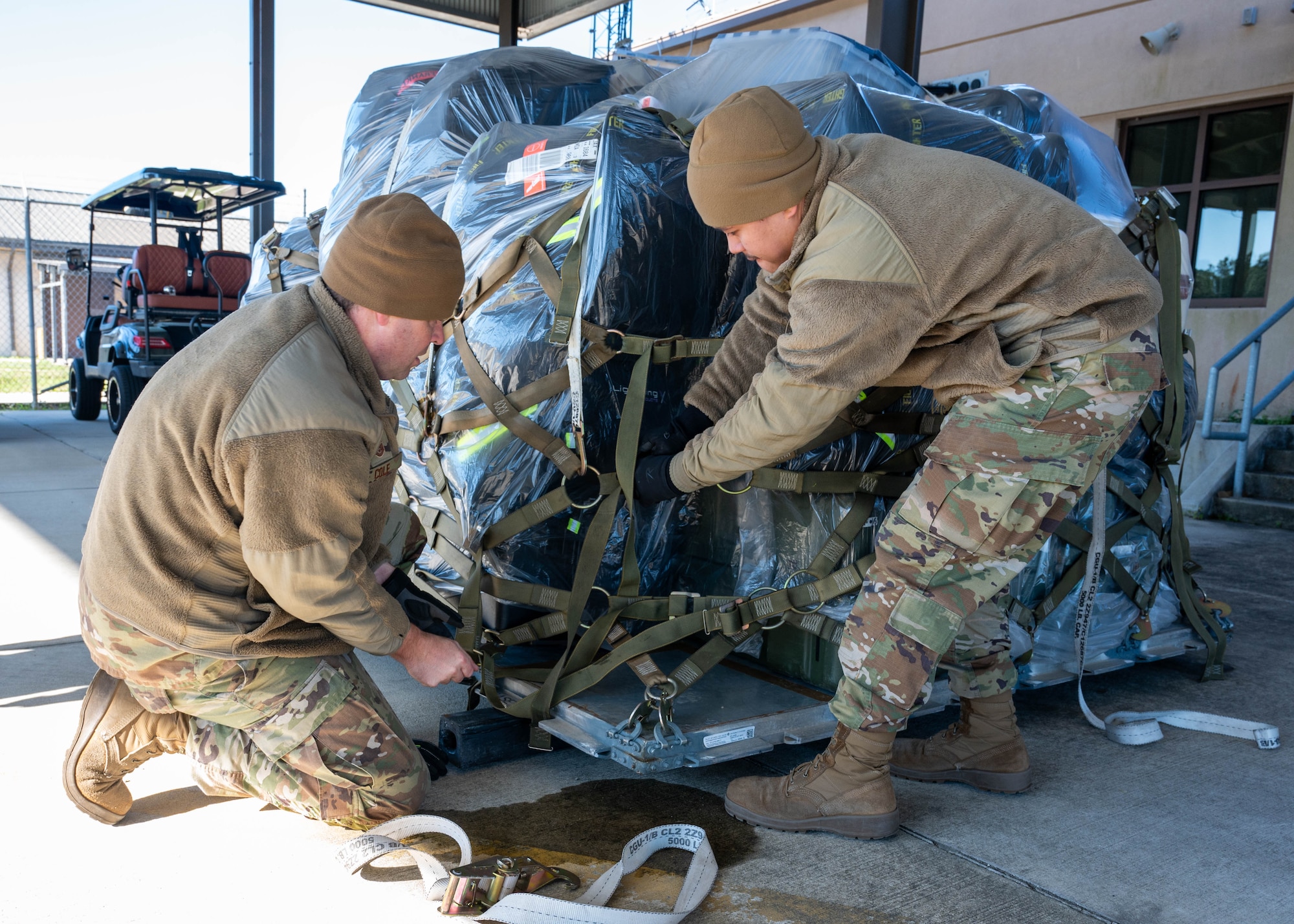 Photo of personnel tightening straps on a pallet.