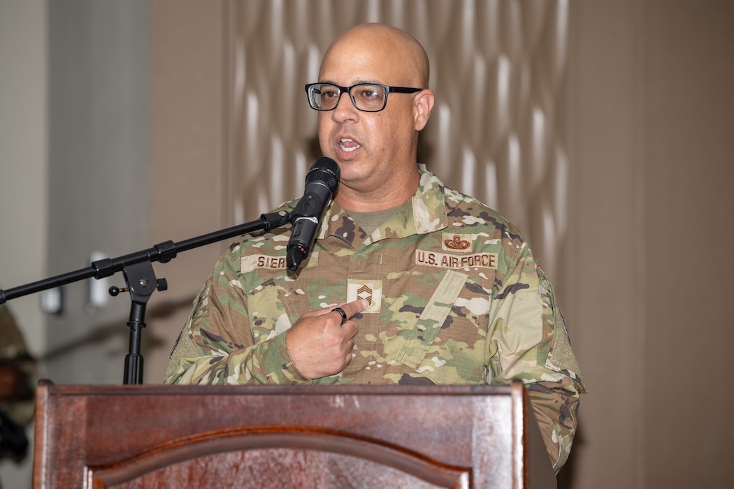 A man wearing camouflaged military uniform speaks into a microphone behind a podium