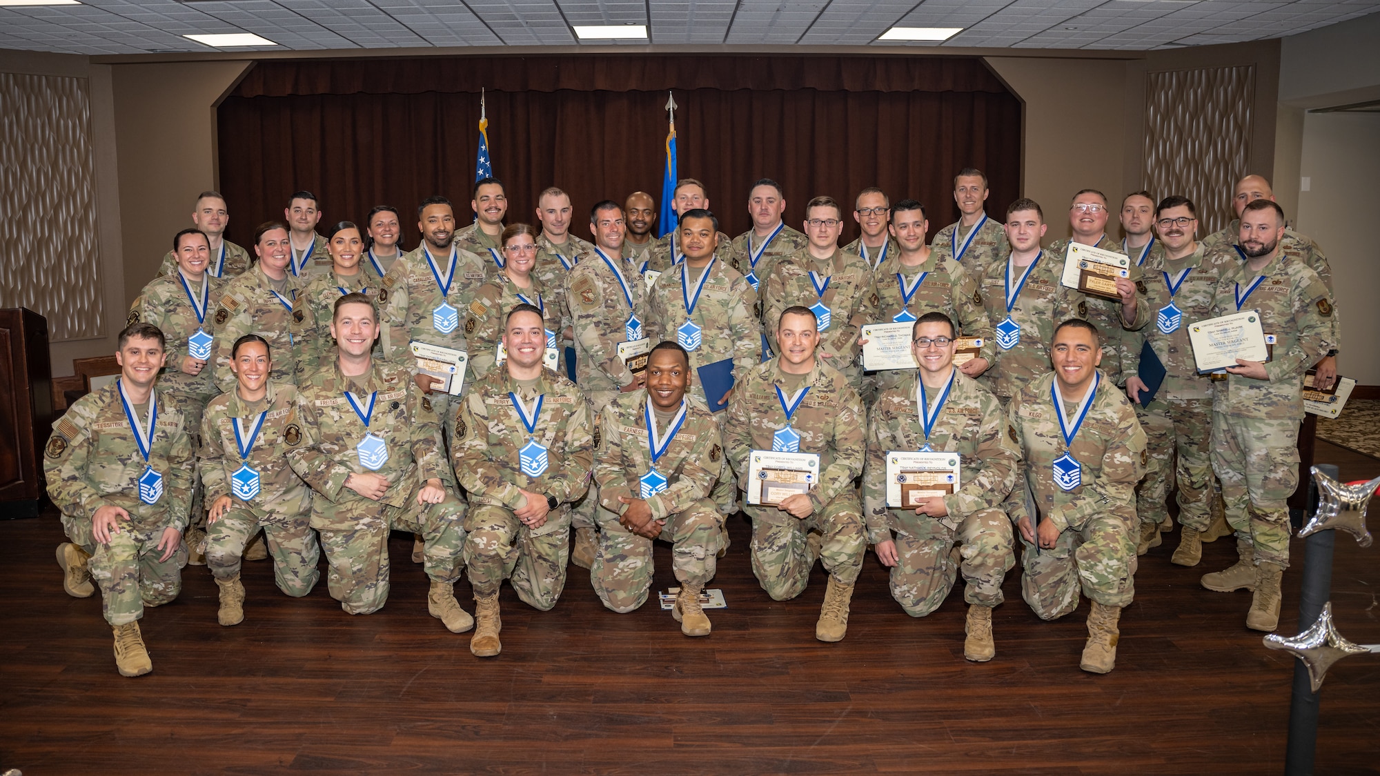 A large group of camouflaged uniformed military members pose for a photo