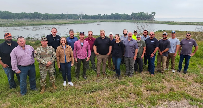 Several people stand lined up in the grass in front of a lake and smile.