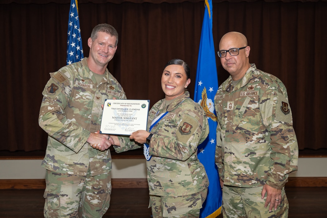 Three camouflaged uniformed military members pose for a photo