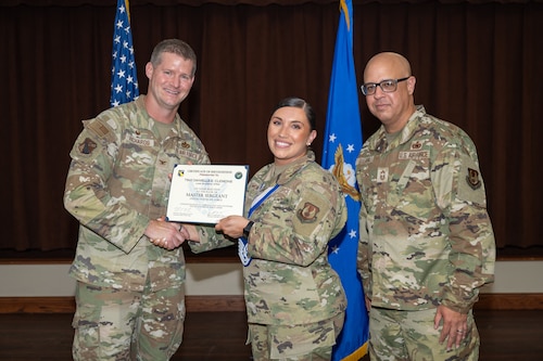 Three camouflaged uniformed military members pose for a photo