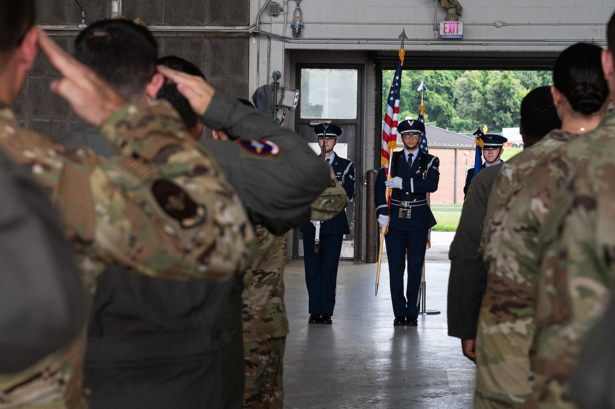 A group of airmen salute towards the American flag carried by the base honor guard, during the national anthem.
