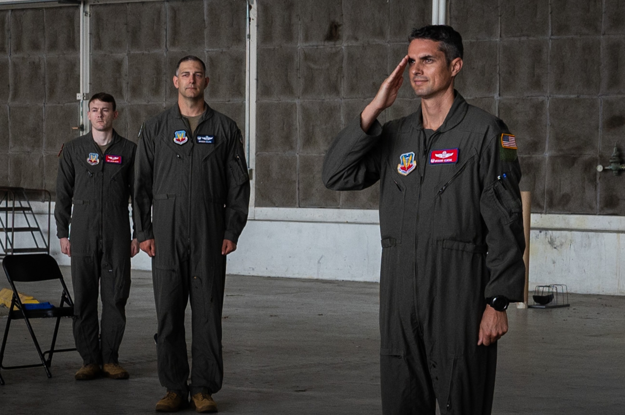 A man salutes as two other men stand behind him.