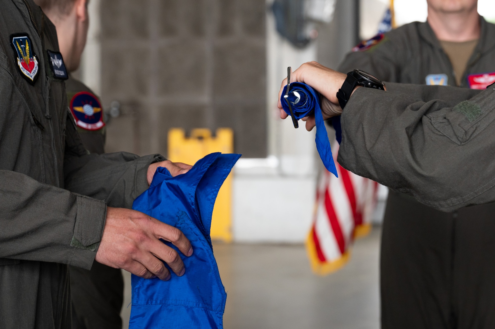 A man rolls up a guidon flag, while another man holds the sheath fabric.
