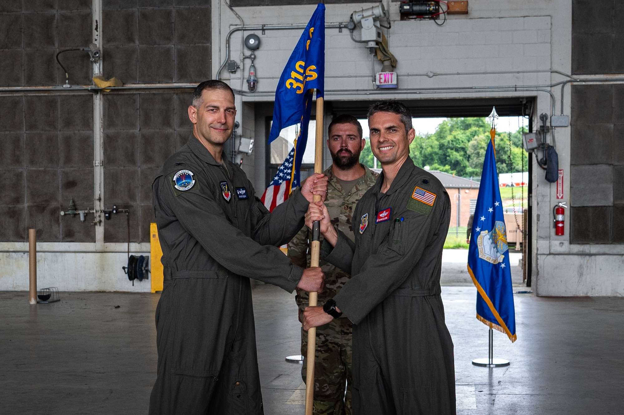 Two men stand on different sides as they hold a guidon in the center of them.