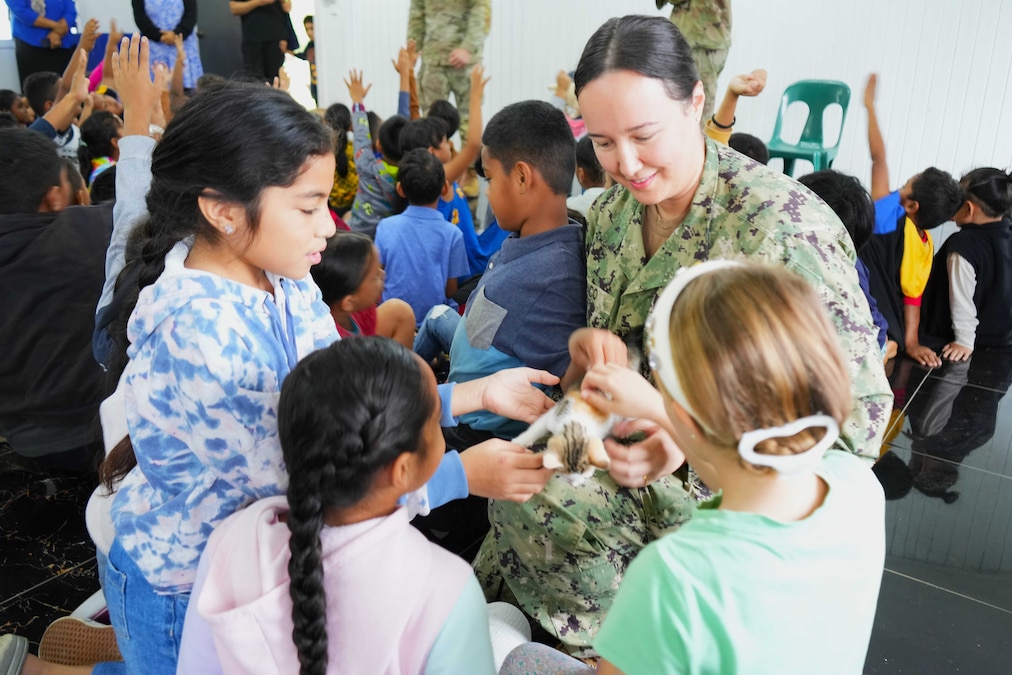 A sailor holds a kitten as three children reach out, while other children stand behind.