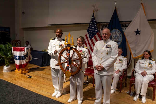250616-N-JC800-1071 BETHESDA, Md. (June 12, 2025) - Lt. Cmdr. Ato Anderson, Finacial and Material Managment Training Course Director, and Command Master Chief Owen Hondorf, present ed a ships wheel to Capt. Katharine Shobe, commanding officer of Naval Medical Leader and Professional Development Command, during NMLPDC's Change of Command Ceremony, Jun. 12. (U.S. Navy photo by Mass Communication Specialist 1st Class Heath Zeigler/Released)