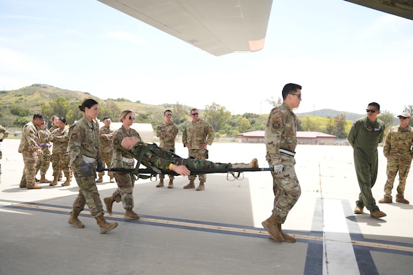 Air Force medical personnel carry a simulated casualty towards a C-130 aircraft during aeromedical evacuation training at Camp Pendleton, California, May 12, 2025. The integrated training with Expeditionary Medical Facility (EMF) conducted at Naval Expeditionary Medicine Warfighter Development Center, focused on safe litter movement and handoff procedures to fixed-wing aircrew members for rapid patient evacuation. (U.S. Navy photo by Petty Officer 2nd Class Moira Esquivel)
