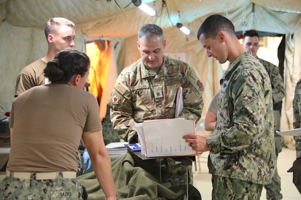 Maj. Michael Schibler (center), reviews medical documentation with Lt. Cmdr. Adam Will (right), family medicine physician, Expeditionary Medicine Facility Juliet (EMF-J), Lt. Cmdr. Nevin Yazici (left) , registered nurse, EMF-J,  and Hospital Corpsman 2nd Class Carson Gorham (left), general duty corpsman, EMF-J,  during a field training exercise at Naval Expeditionary Medicine Warfighter Development Center (NEMWDC), May 11, 2025. The teams collaborated on patient tracking and triage procedures in a simulated combat casualty care scenario. (U.S. Navy photo by Petty Officer 2nd Class Kwame Obengyeboah)