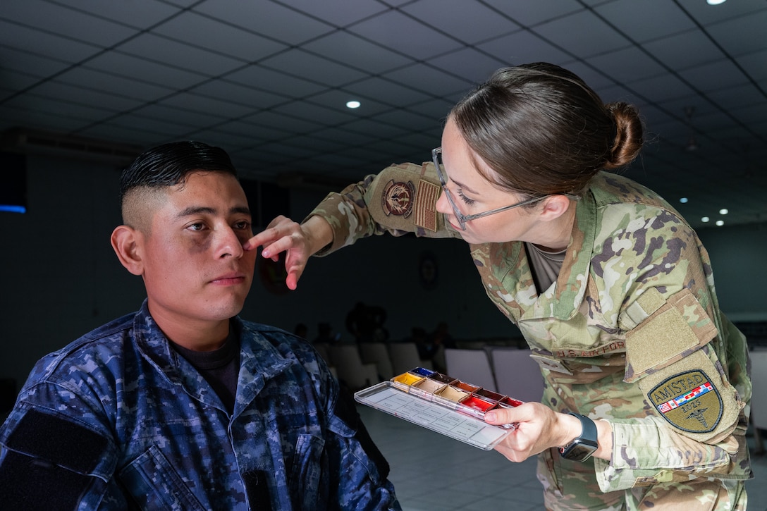 U.S. Air Force Senior Airman Marissa Poindexter, 944th Aeromedical Staging Squadron medical technician, applies simulated injuries to the face of an El Salvador Primera Brigada Aerea member prior to a training exercise in Ilopango, El Salvador, June 20, 2025. The simulated tactical combat casualty care was part of the AMISTAD campaign, intended to promote cooperation between healthcare professionals of U.S. and partner nations in Central and South America. (U.S. Air Force photo by Tech. Sgt. Justin Norton)