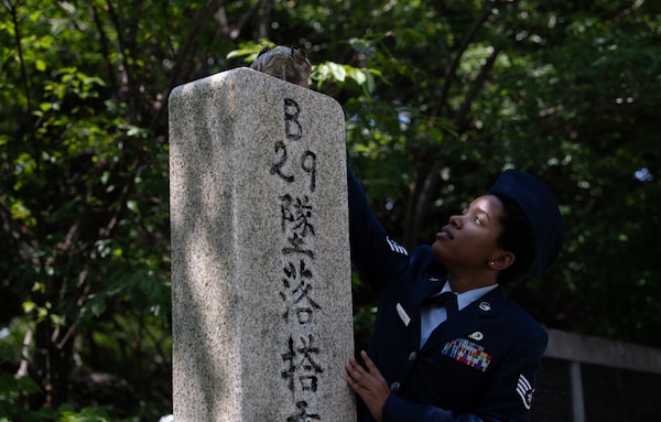 An Airman dressed in their blue dress uniform and flight cap reaches pours whiskey out of a canteen over a stone monument.
