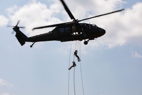 Two people are rappelling out of an airborne helicopter.