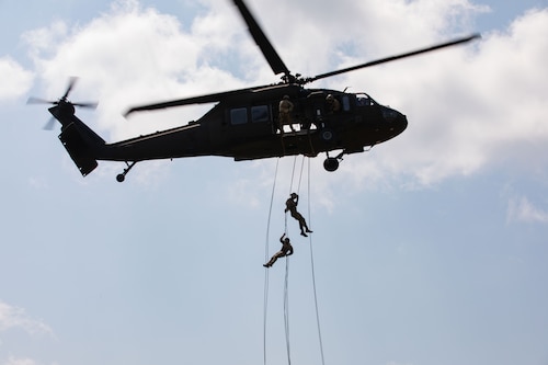 Two people are rappelling out of an airborne helicopter.