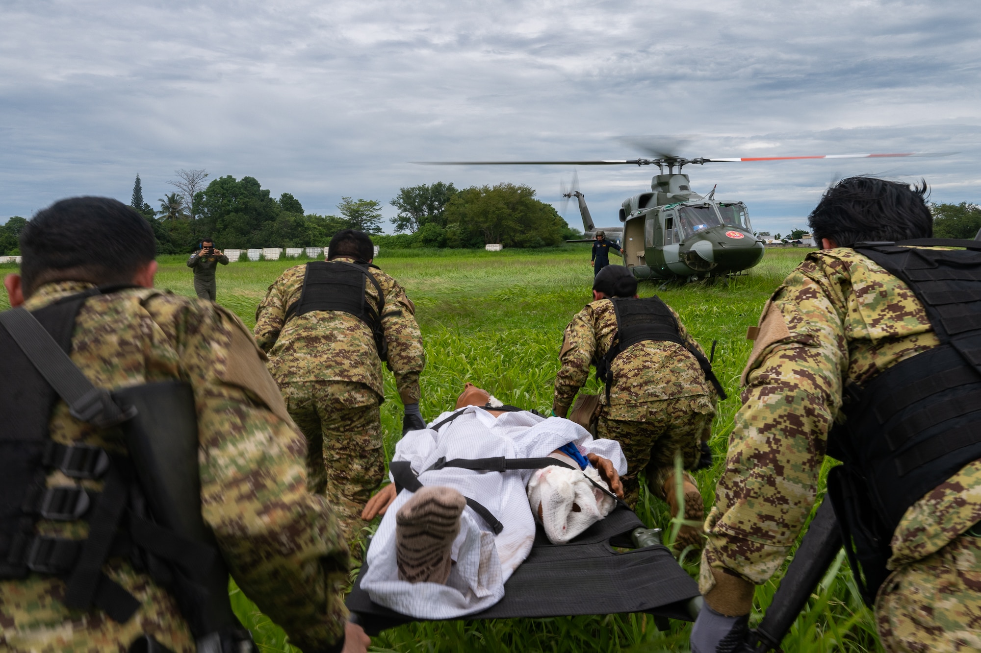 An El Salvador Primera Brigada Aérea team carries a litter towards a Bell 412 helicopter during a simulated combat casualty training scenario in Ilopango, El Salvador, June 20, 2025. Teams treated simulated injuries on the medical training mannequin and prepared it for aeromedical transport during the AMISTAD campaign, an ongoing mission intended to strengthen relations between U.S. and partner nations by training together in resource-constrained environments. (U.S. Air Force photo by Tech. Sgt. Justin Norton)