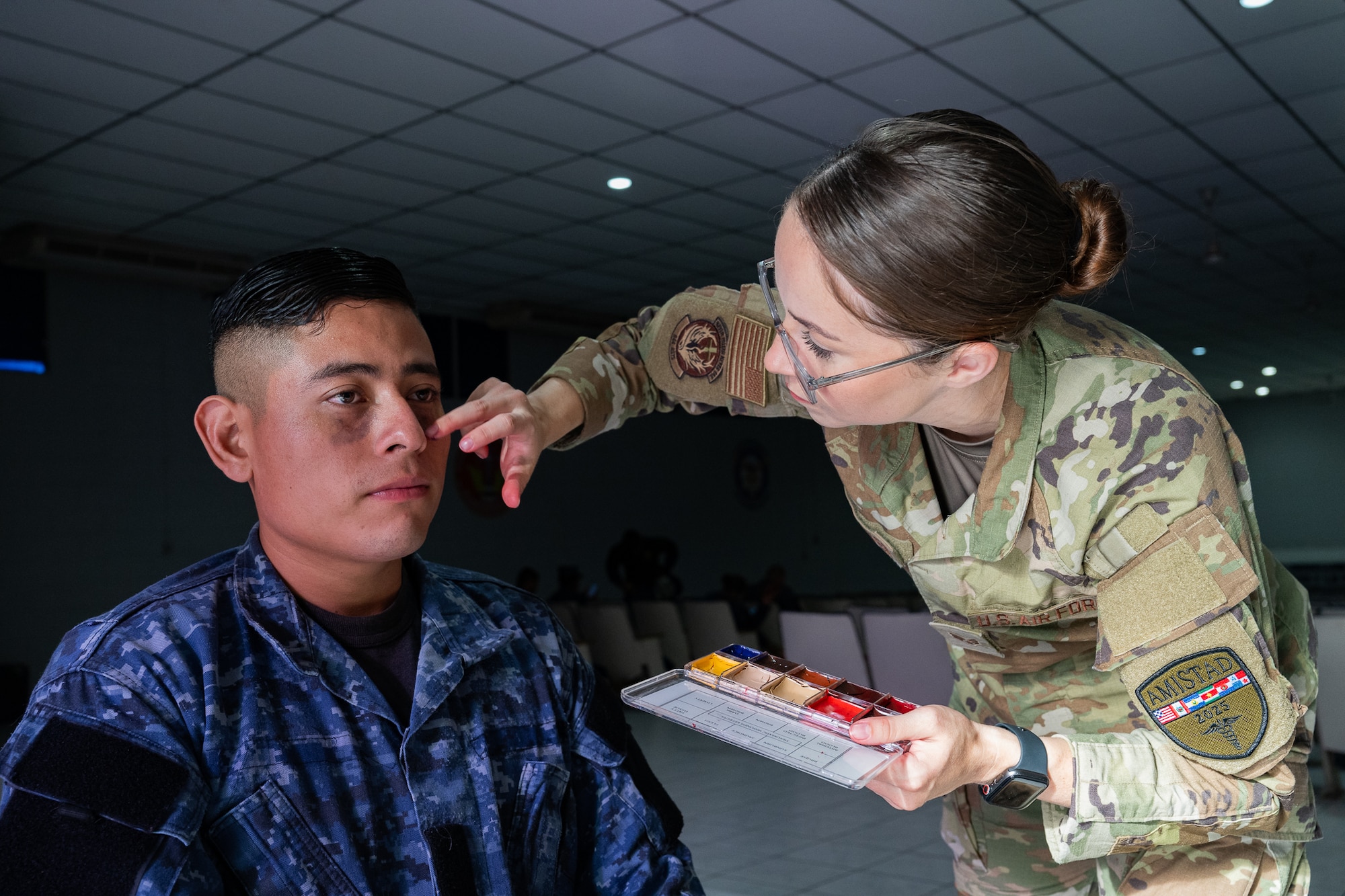 U.S. Air Force Senior Airman Marissa Poindexter, 944th Aeromedical Staging Squadron medical technician, applies simulated injuries to the face of an El Salvador Primera Brigada Aerea member prior to a training exercise in Ilopango, El Salvador, June 20, 2025. The simulated tactical combat casualty care was part of the AMISTAD campaign, intended to promote cooperation between healthcare professionals of U.S. and partner nations in Central and South America. (U.S. Air Force photo by Tech. Sgt. Justin Norton)