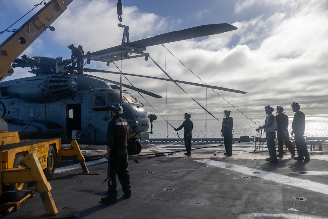 U.S. Marines with Marine Tiltrotor Squadron 265 (Rein.), 31st Marine Expeditionary Unit, lift a rotor blade to a CH-53E Super Stallion assigned to VMM 265 (Rein.) during aircraft maintenance aboard amphibious assault ship USS America (LHA 6) in the Coral Sea, June 25, 2025. Marines with VMM 265 (Rein.) perform rotor maintenance on an amphibious assault ship to a CH-53E Super Stallion, demonstrating versatility and ever-expanding capabilities in a forward deployment environment. The 31st MEU is operating aboard ships of the USS America Amphibious Ready Group in the 7th Fleet area of operations, the U.S. Navy’s largest forward-deployed numbered fleet, and routinely interacts and operates with allies and partners in preserving a free and open Indo-Pacific region. (U.S. Marine Corps photo by Sgt. Peter Rawlins)