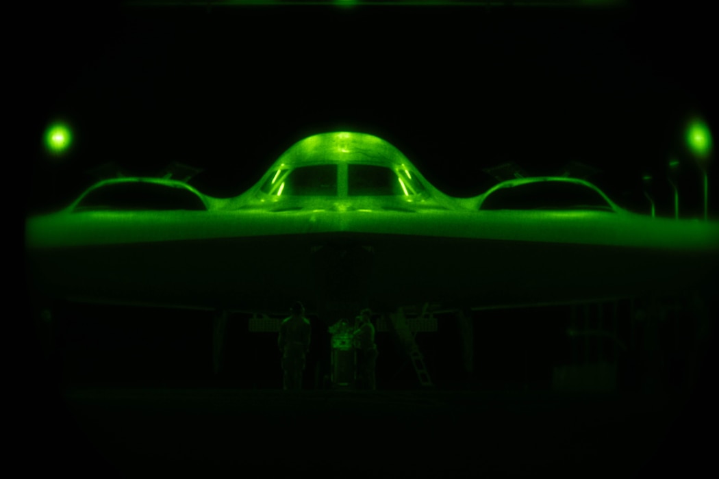 A B-2 Spirit stealth bomber aircraft bathed in green light as viewed through a night-vision lens.
