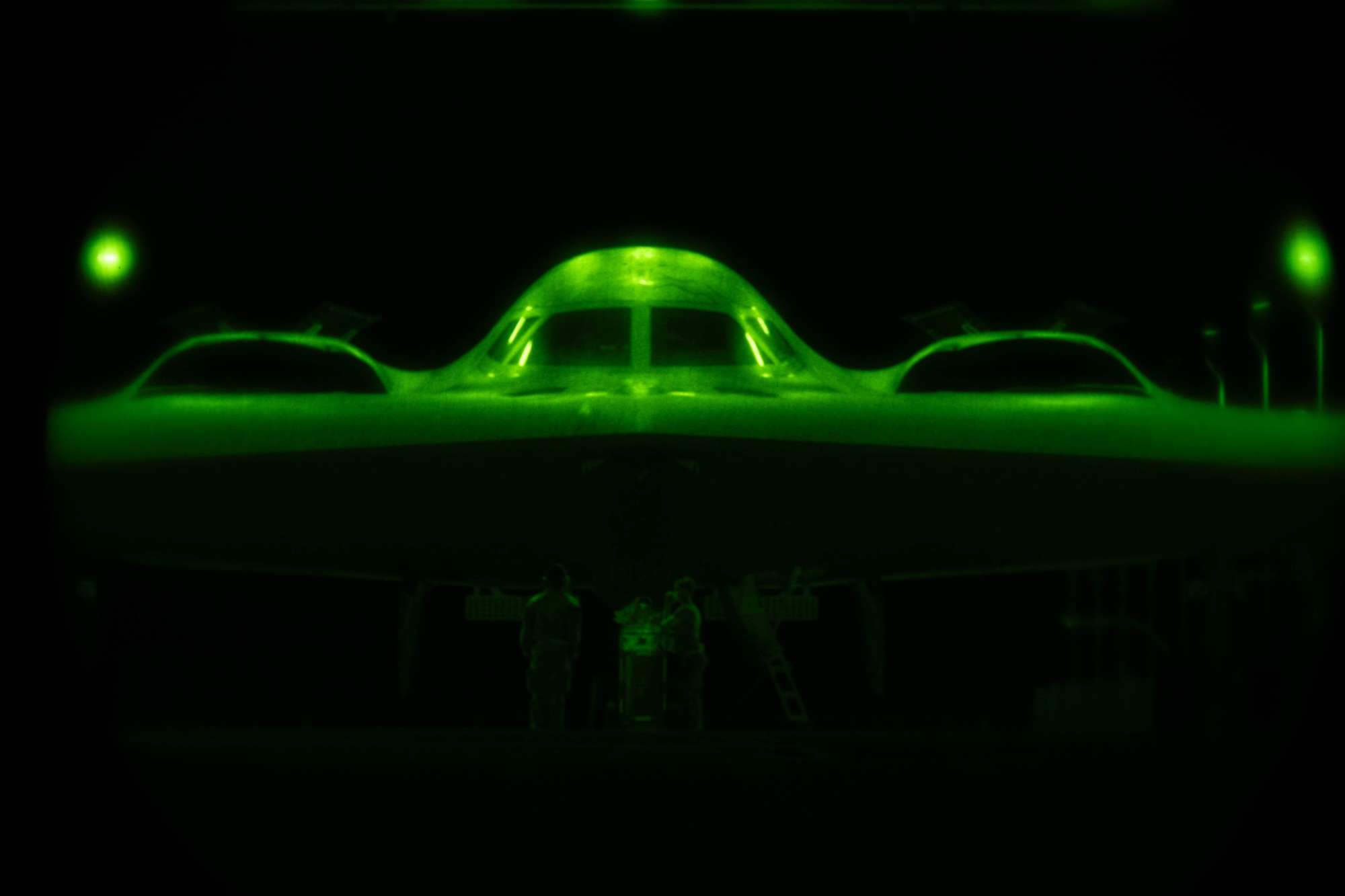 A B-2 Spirit stealth bomber aircraft bathed in green light as viewed through a night-vision lens.
