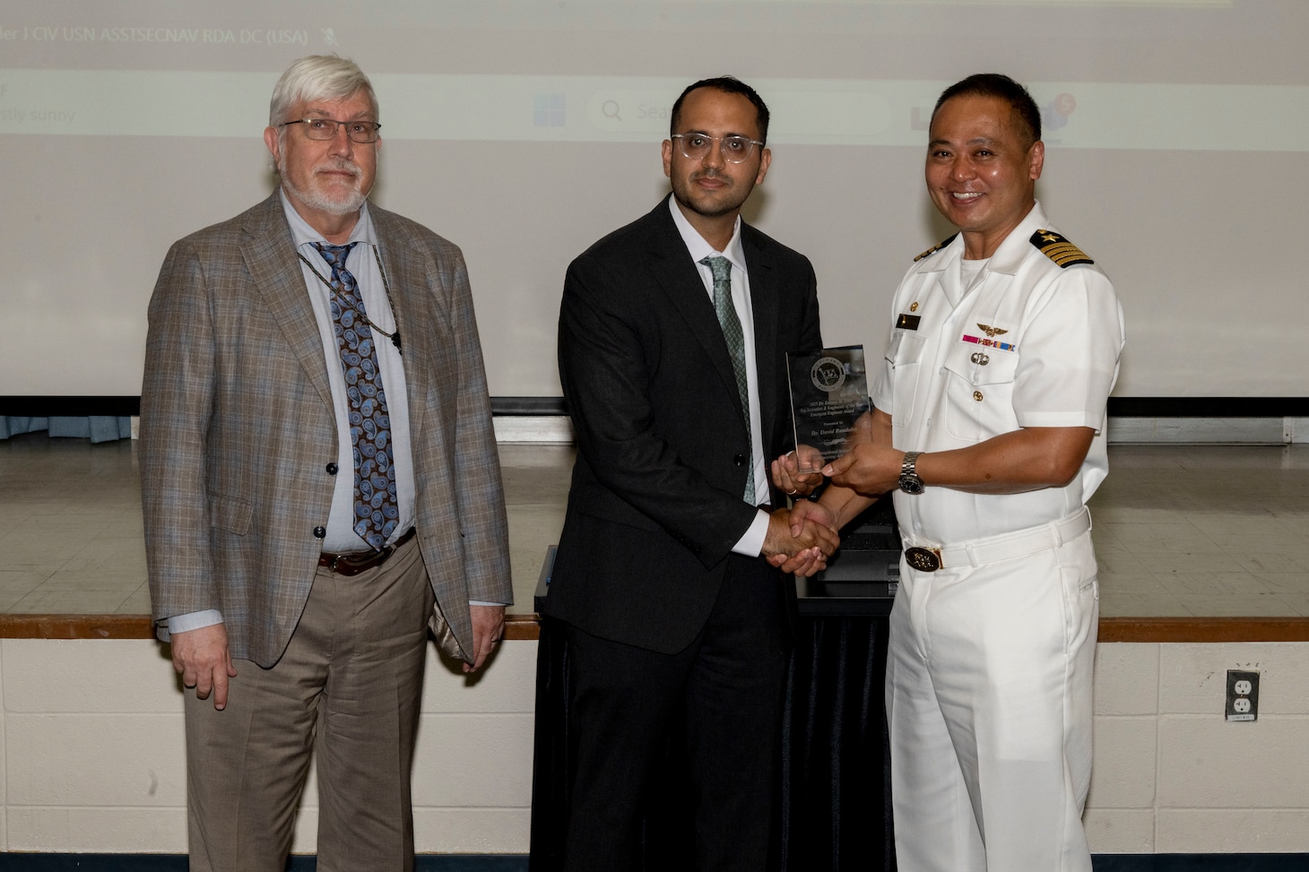 Three gentlemen stand together holding an award