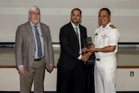 Three gentlemen stand together holding an award