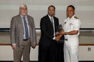 Three gentlemen stand together holding an award