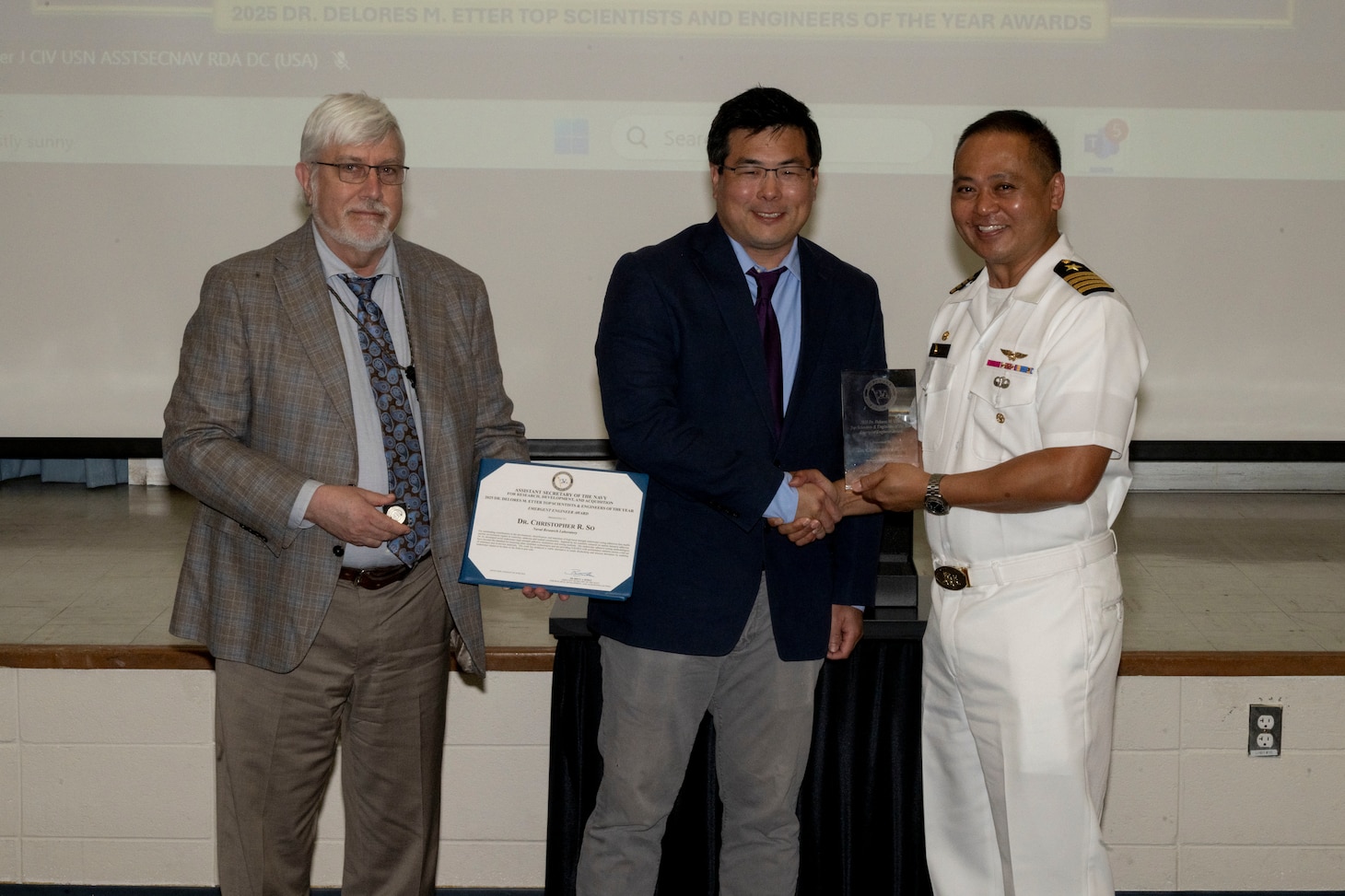 Three gentlemen stand together holding an award