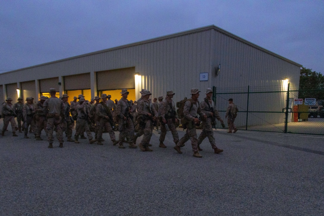 Marines carrying rifles walk as a group in darkened conditions with a building in the background.