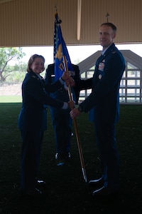 U.S. Air Force Col. Angelina Maguinness, 17th Training Wing commander, passes the guidon to Col. Nathan Olsen, 17th Mission Support Group commander, during the change of command ceremony at the 17th Security Forces Squadron kennels, Goodfellow Air Force Base, Texas, June 26, 2025. The passing of the guidon is a military tradition that dates back to the time of Frederick the Great of Prussia. (U.S. Air Force photo by Airman 1st Class Brian Lummus)
