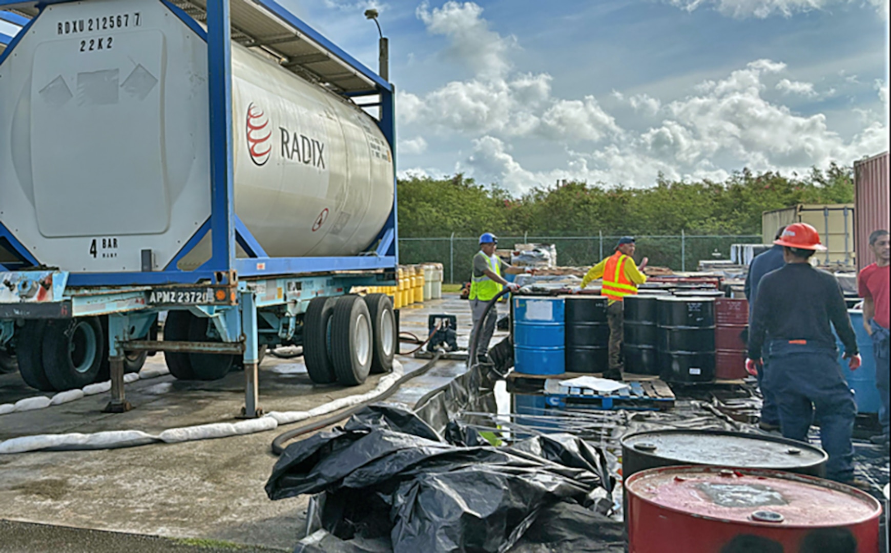 Men use a pump to empty barrels into a large tank in an industrial setting.